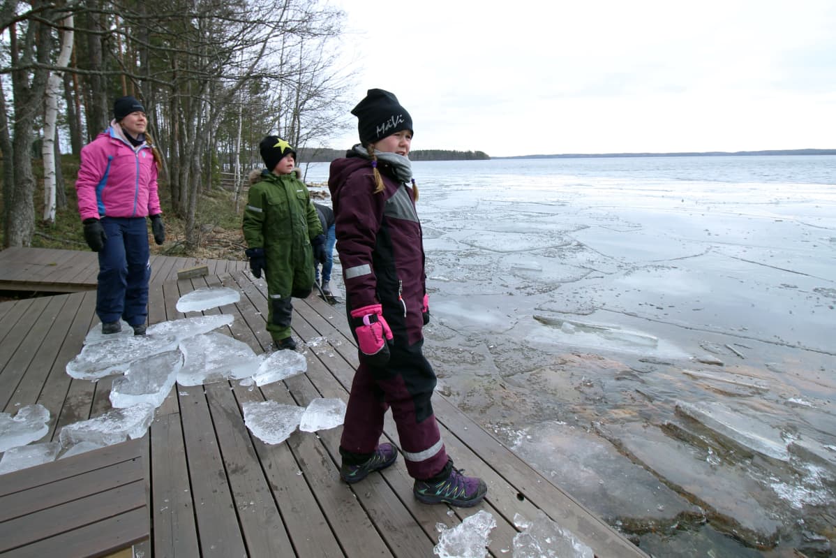 Perhe leikkii jääpaloilla järven rannassa.