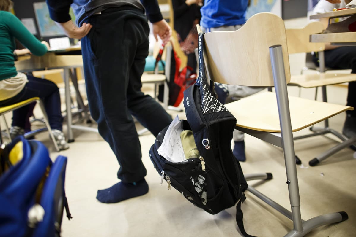 Aukinainen koulureppu roikkuu tuolilla ala-asteen luokatilassa.