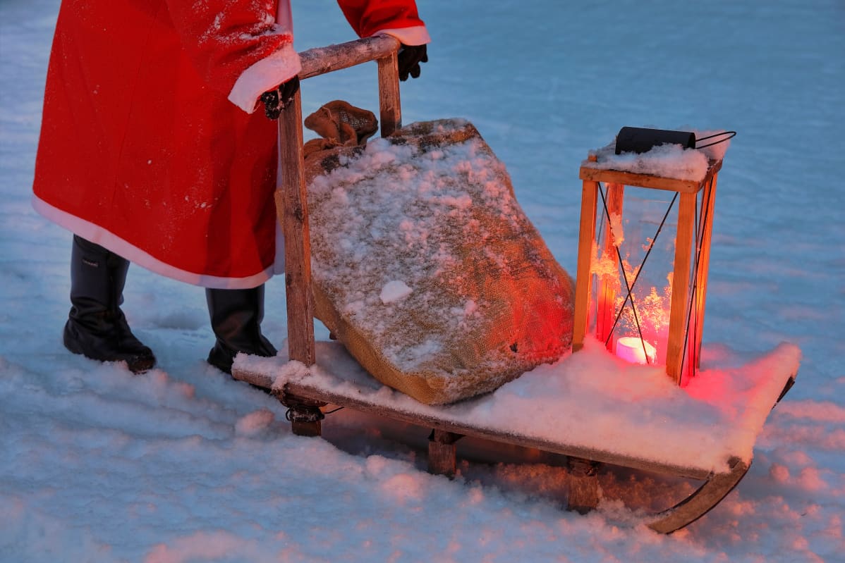Joulupukin jalat ja kelkka, jossa on lyhty ja lahjasäkki.