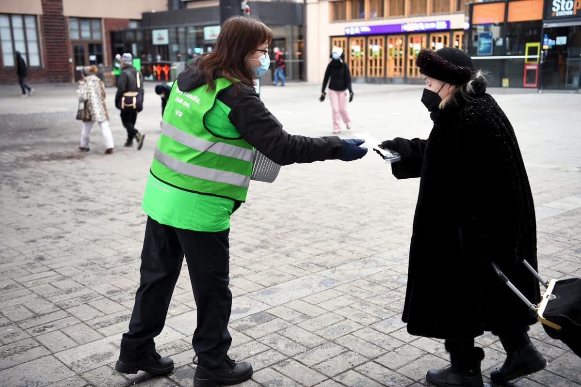 VR:n henkilökunta jakaa matkustajille kasvomaskeja Helsingin Rautatieasemalla.