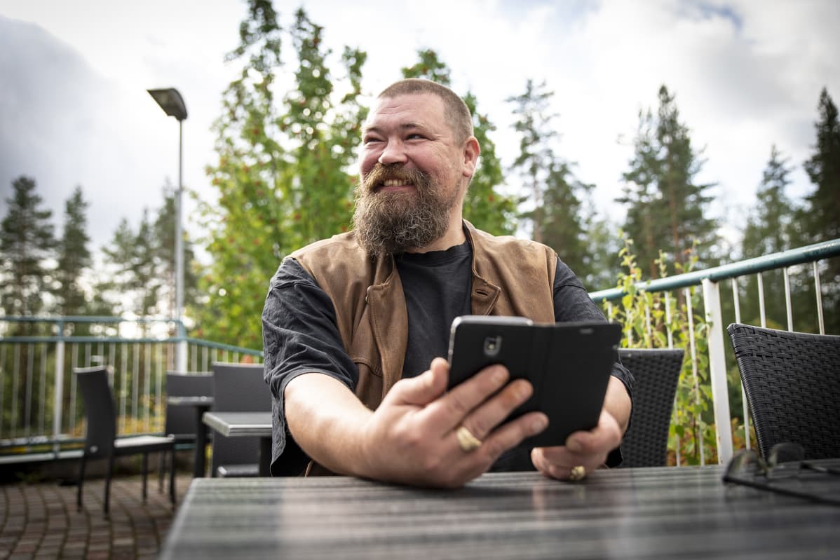 Kaj Niemitalo istuu ja hymyilee pöydän äärellä.