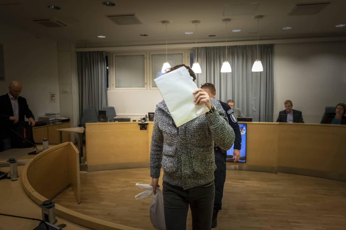 Rahanpesusta syytetty peittää kasvonsa oikeudenkäynnin alkaessa.