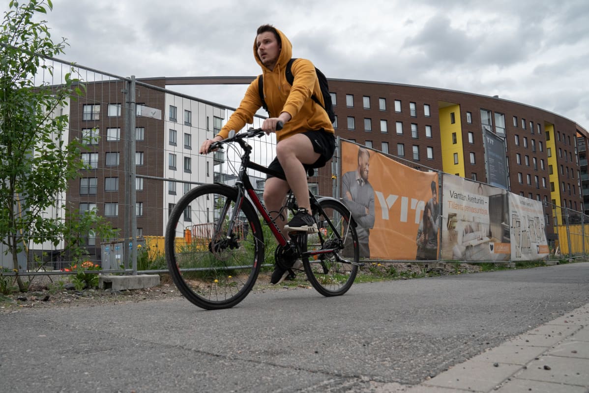Palveluja saa vielä odottaa Vantaan Kivistössä. Naapurustokaan ei ole ihan vielä valmis. Alueelle kaavaillaan lisärakentamista jopa 30 000 uudelle asukkaalle. Nyori mies pyöräilee työmaaaitojen edessä.