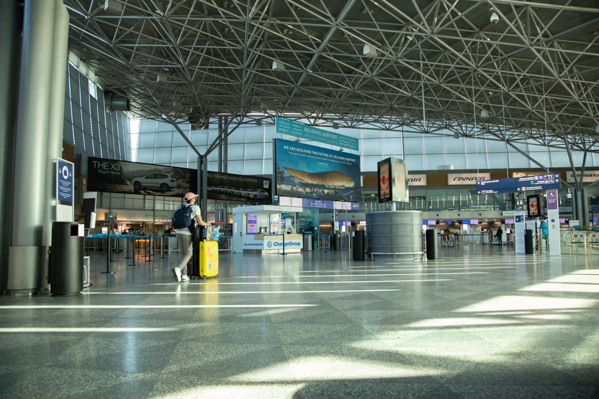 Helsinki-Vantaa lentoaseman terminaali 2 lähtöaula. Koko aula on lähes tyhjä. Yksi henkilö työntää keltaista pyörällistä matkalaukkuaan kohti turvatarkastusta.