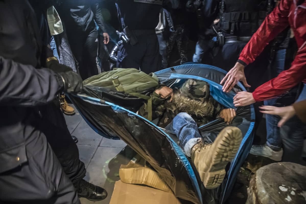 Poliisit ja mielenosoittajat kiskovat telttaa, josta näkyy jalka.