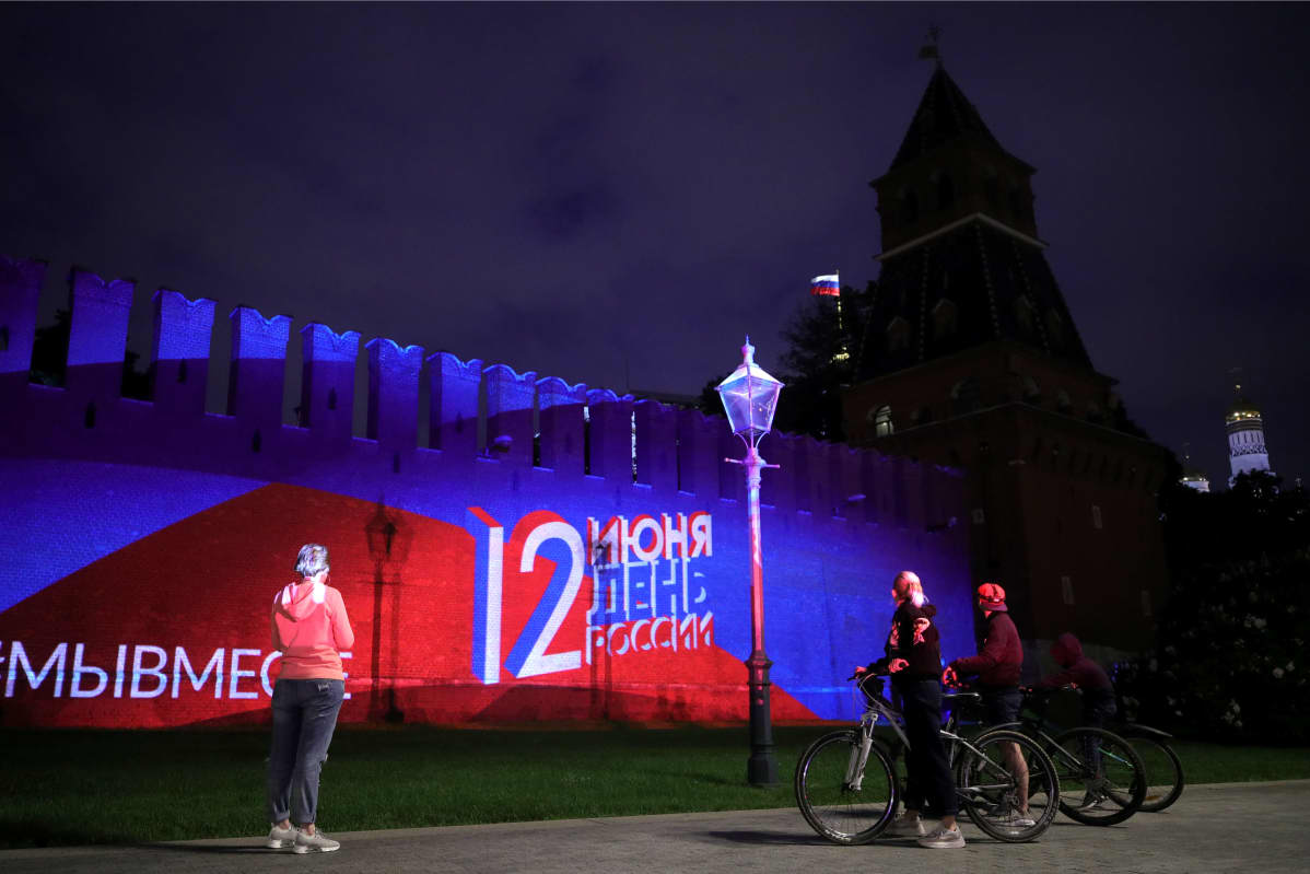 Ihmiset ihailevat Venäjän kansallispäivän kunniaksi tehtyä valoshouta Kremlin muurissa.