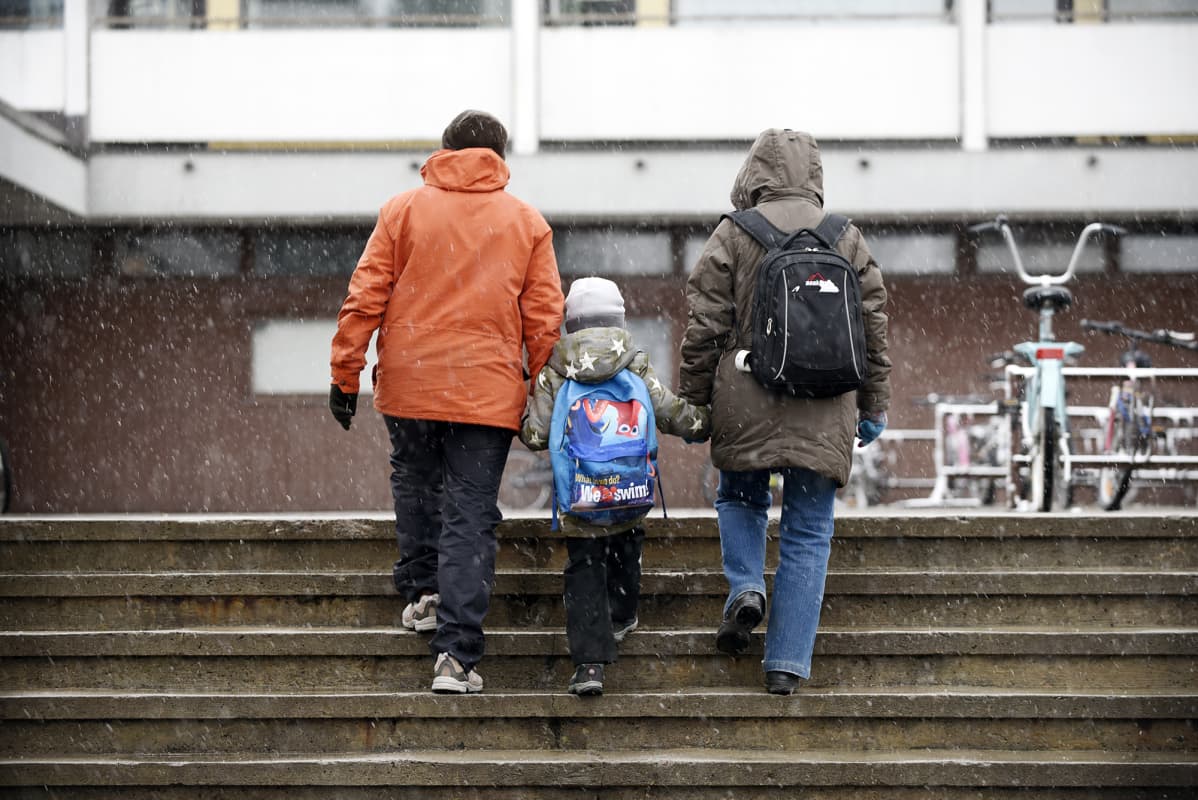 Perhe kävelee ulkoportaissa lumisateessa.