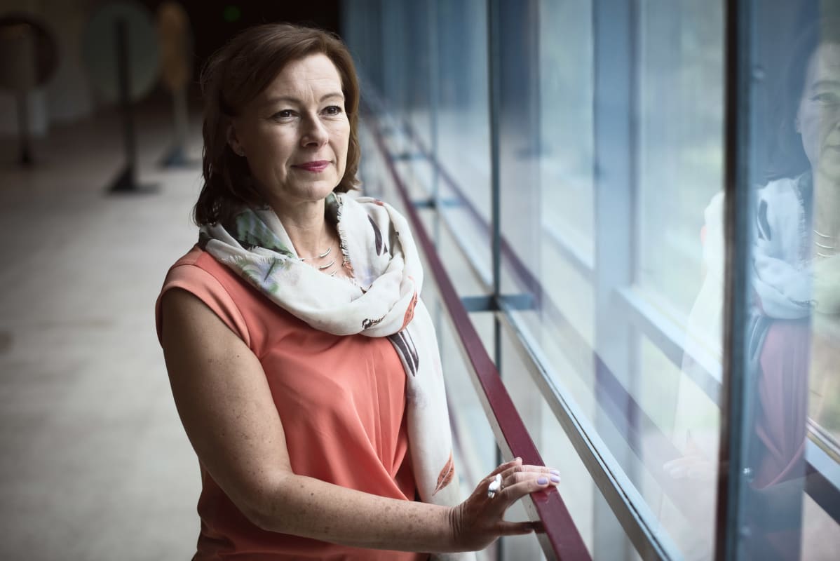 Susanna Tommila seisoo ikkunarivistön vieressä. Katsoo ulos.