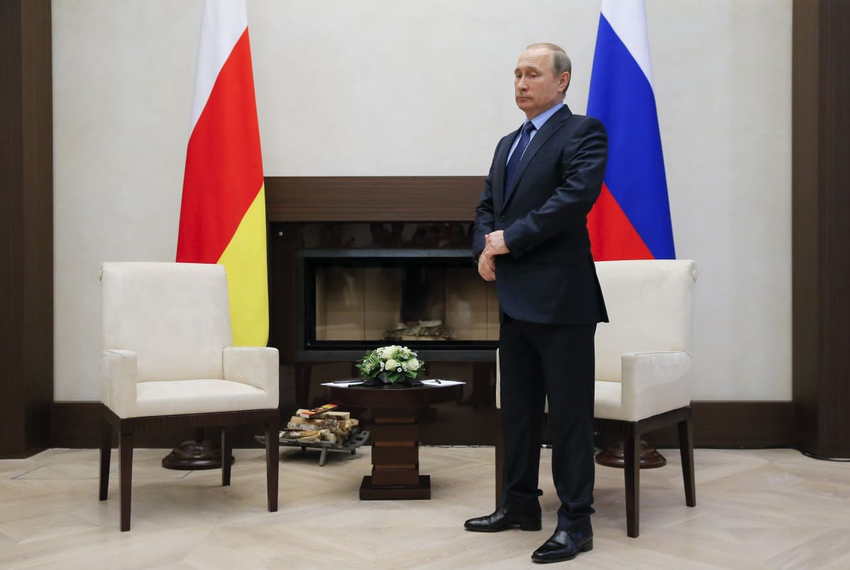 Putin seisoo huoneessa, jossa on Venäjän ja Etelä-Ossetian liput, kaksi nojatuolia ja takka.