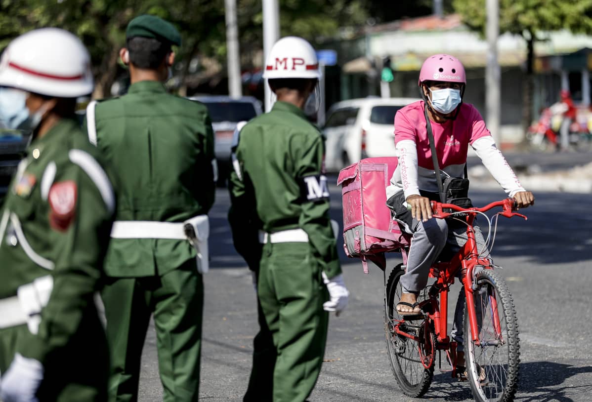 Ruokalähetti ajaa polkupyörällä sotilaspoliisien vieressä Yangonissa.