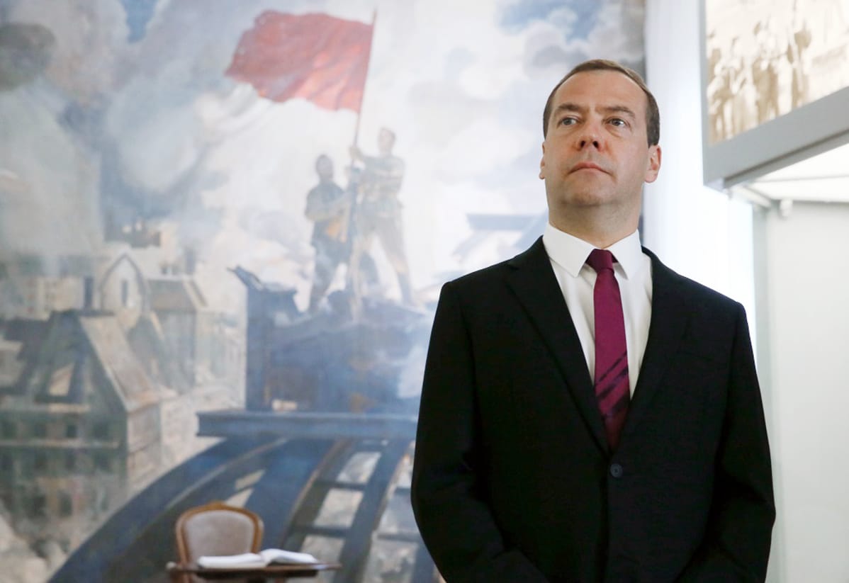 Dmitri Medvedev seisoo seinämaalauksen edessä Smolenskin alueen sotamuseossa ja katsoo kuva-alalla yläoikeaan. Maalauksessa neuvostosotilaat pystyttävät punalippua talon katolle sodasta kärsineessä kaupunkimaisemassa.
