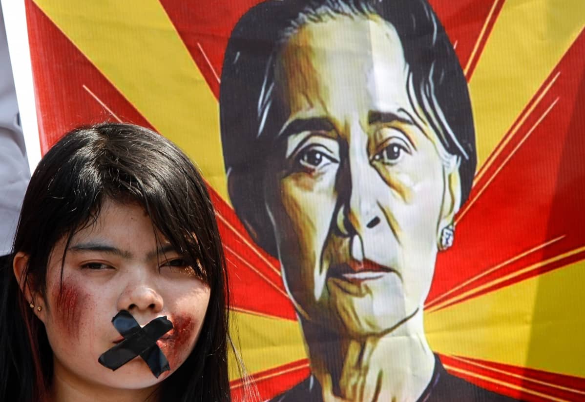 Suu Kyin kannattaja on teipannut suunsa kiinni, taustalla Suu Kyin kuva bannerissa.