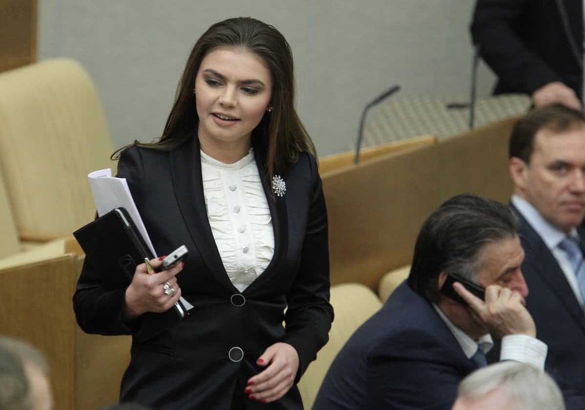 Alina Kabajeva seisoo penkin edessä Venäjän parlamentin alahuoneen istuntosalissa. Kädessä hänellä on kännykkä, tabletti ja papereita.
