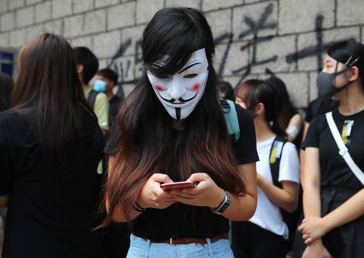 Nainen kirjottaa jotakin kännykällään Guy Fawkes maski kasvoilla