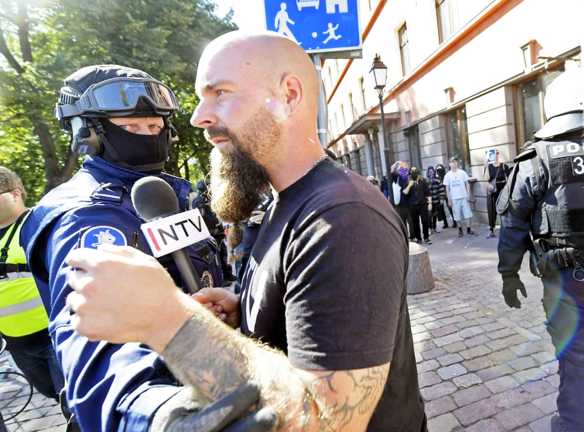 Poliisi estää uusnatsien Pohjoismaisen vastarintaliikkeen NTV-kanavan toimittajana esiintynyttä miestä menemästä vastamielenosoittajien luokse.