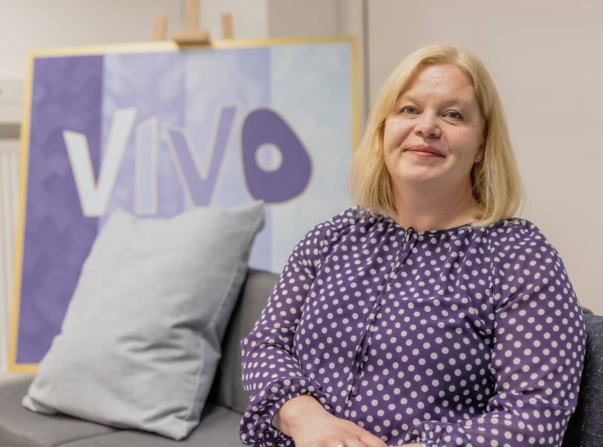 Niina Ojanperä istuu sohvalla. Taustalla Vivo-maalaus.