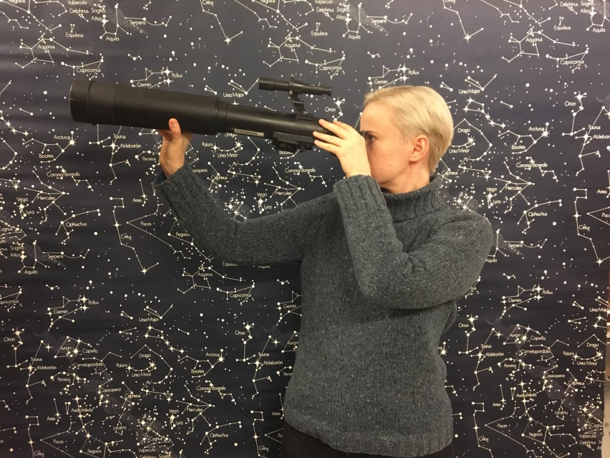 Anne Liljeström katsoo kaukoputkeen taustalla tähtikartta.