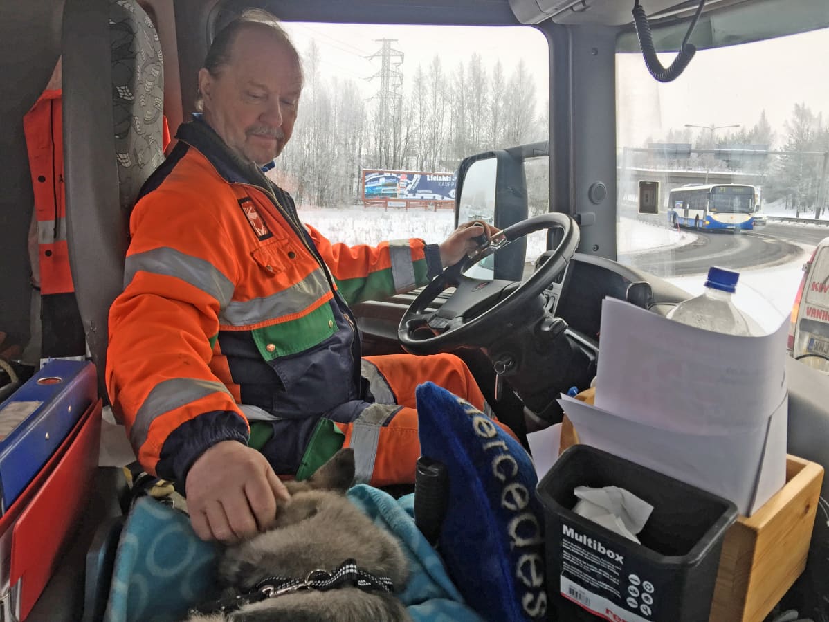 Arto Paltta rapsuttaa pientä koiraa kuorma-auton kyydissä
