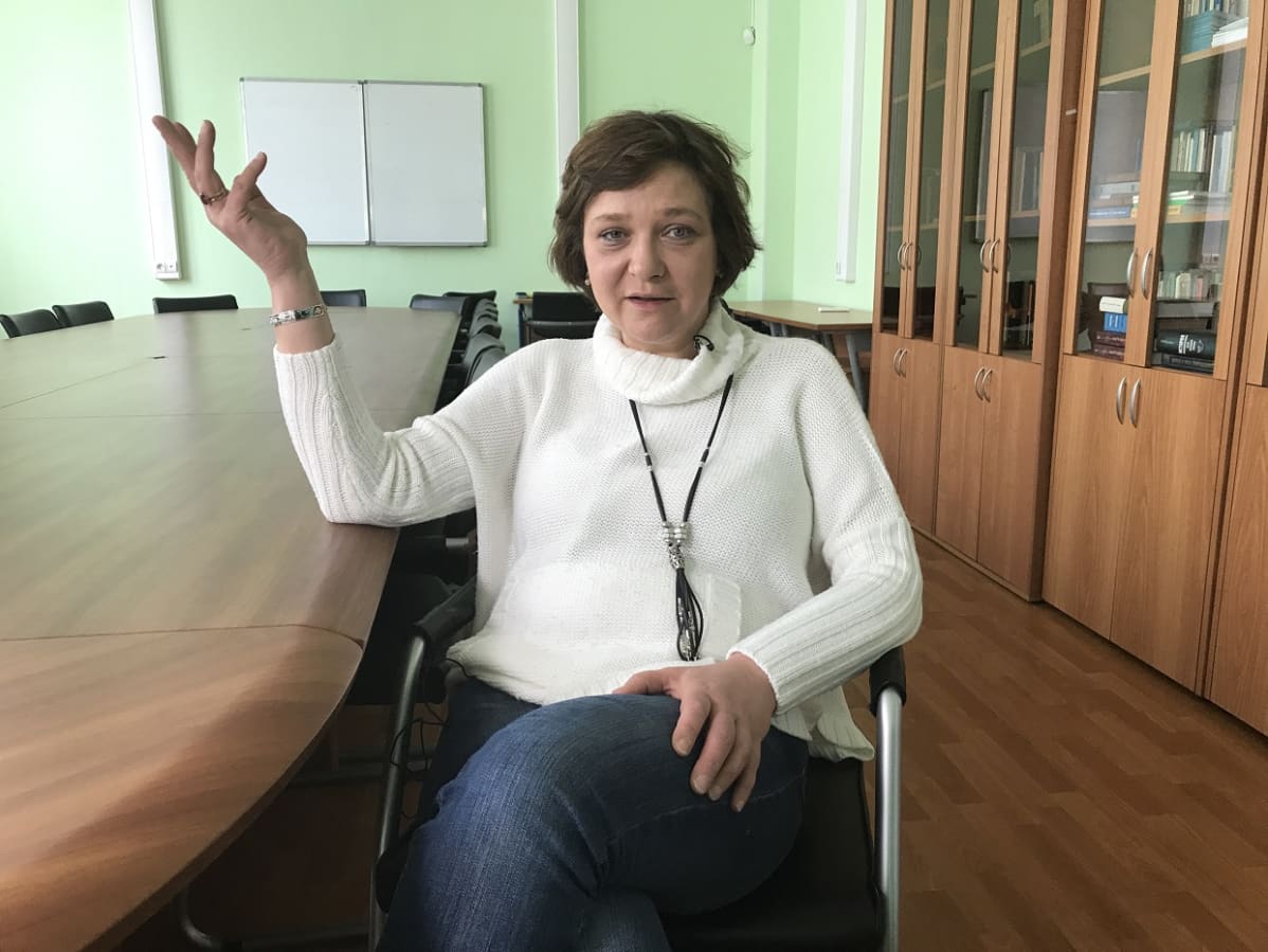 Jelena Panfilova istuu ja nostaa oikeaa kättään ilmaan katsoen kameraan.