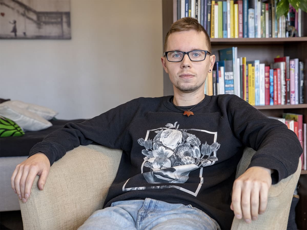 Kestävän hyvinvoinnin kokemusasiantuntija Mikko Valtonen istuu tuolilla kotonaan kirjahyllyn edessä.