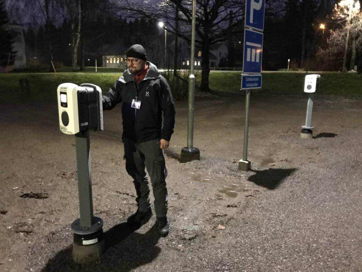 Mies seisoo sähköauton latauspisteen vieressä.
