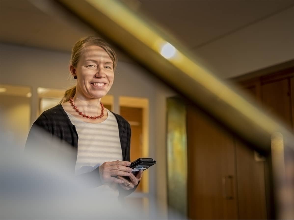 Tanja Oksa pitelee käsissään puhelinta ja hymyilee.