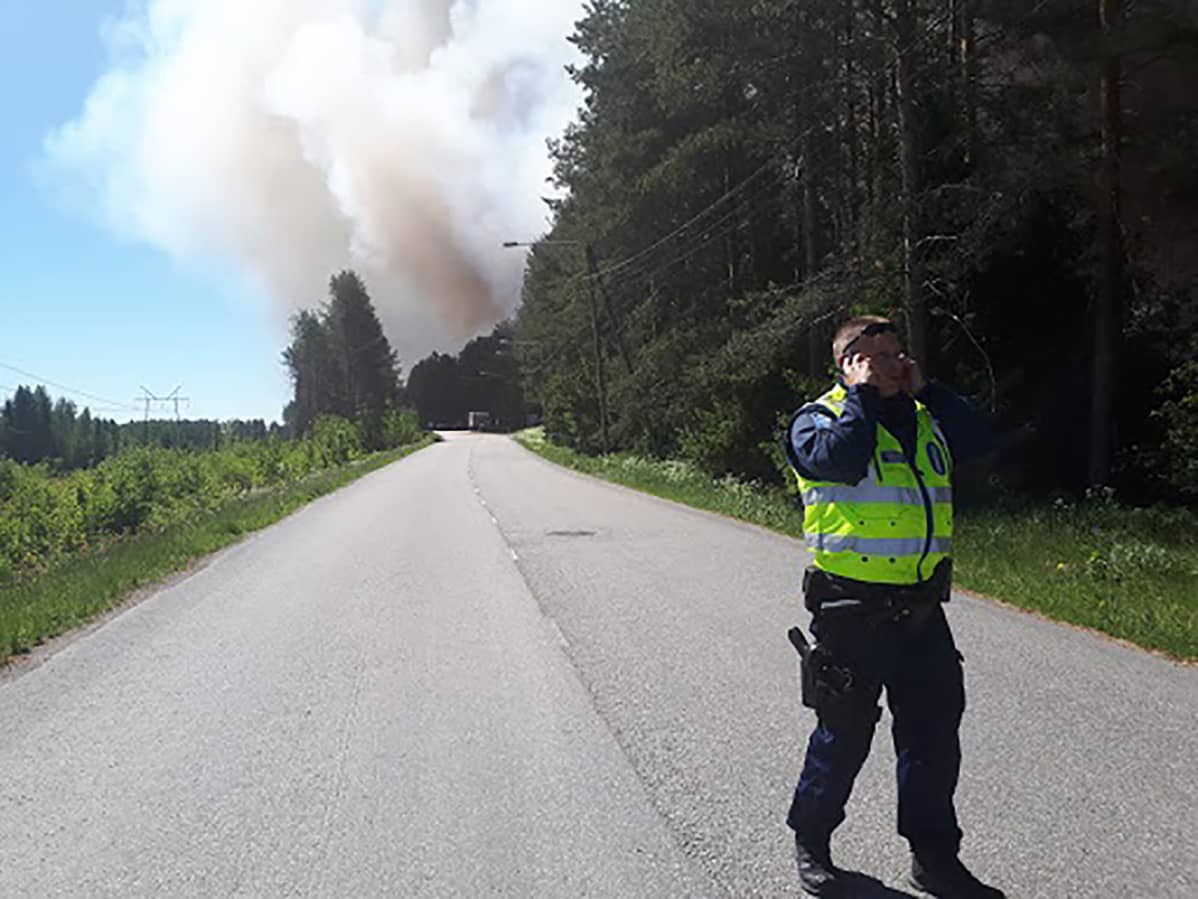 Poliisi tiellä, taustalla tulipalon savupatsas.