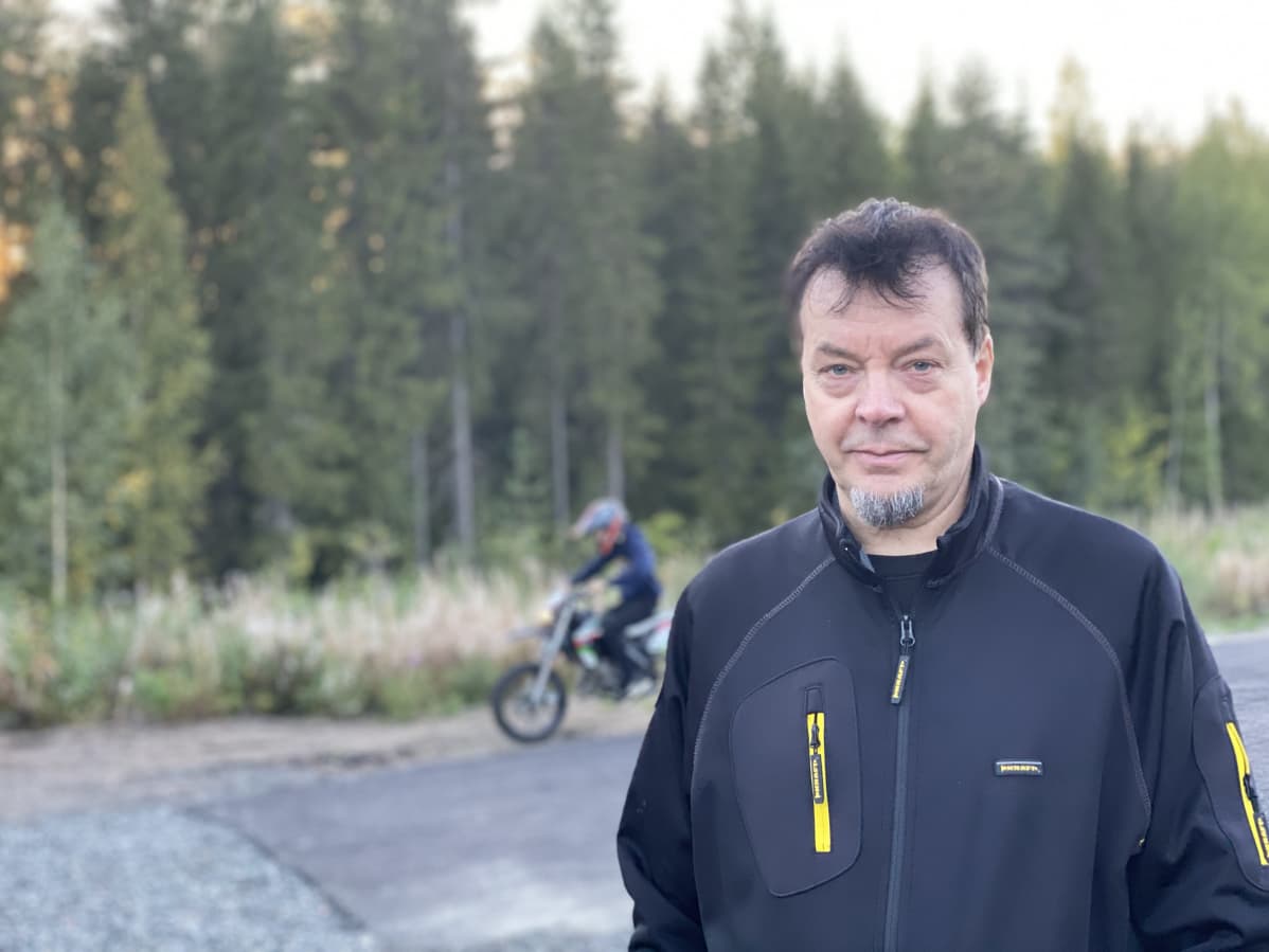 Tiitus Lahti seisoo mopoalueella, Taustalla poika ajaa mopolla.