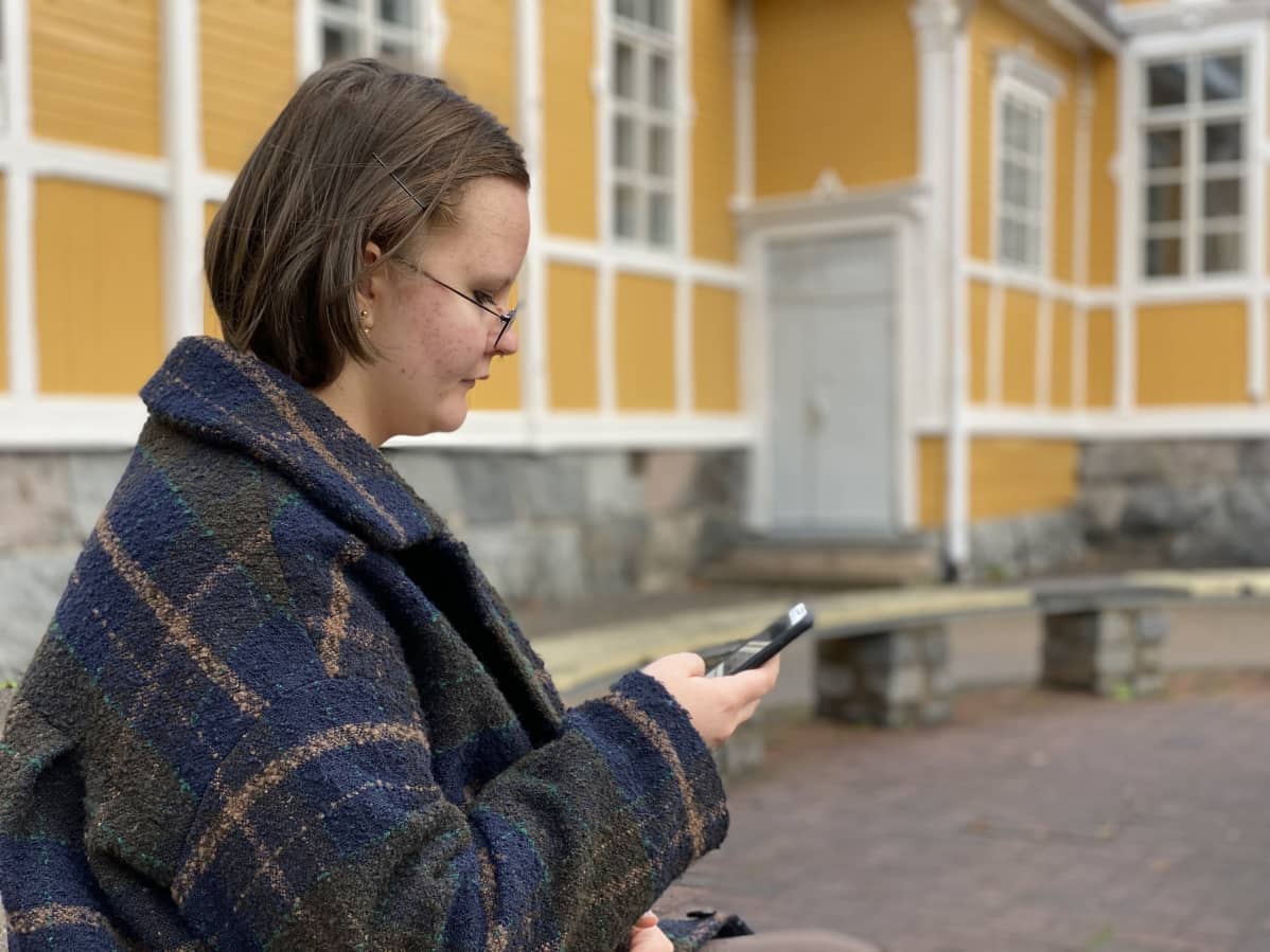 Anetta Kukkonen selaa puhelinta koulun pihalla.
