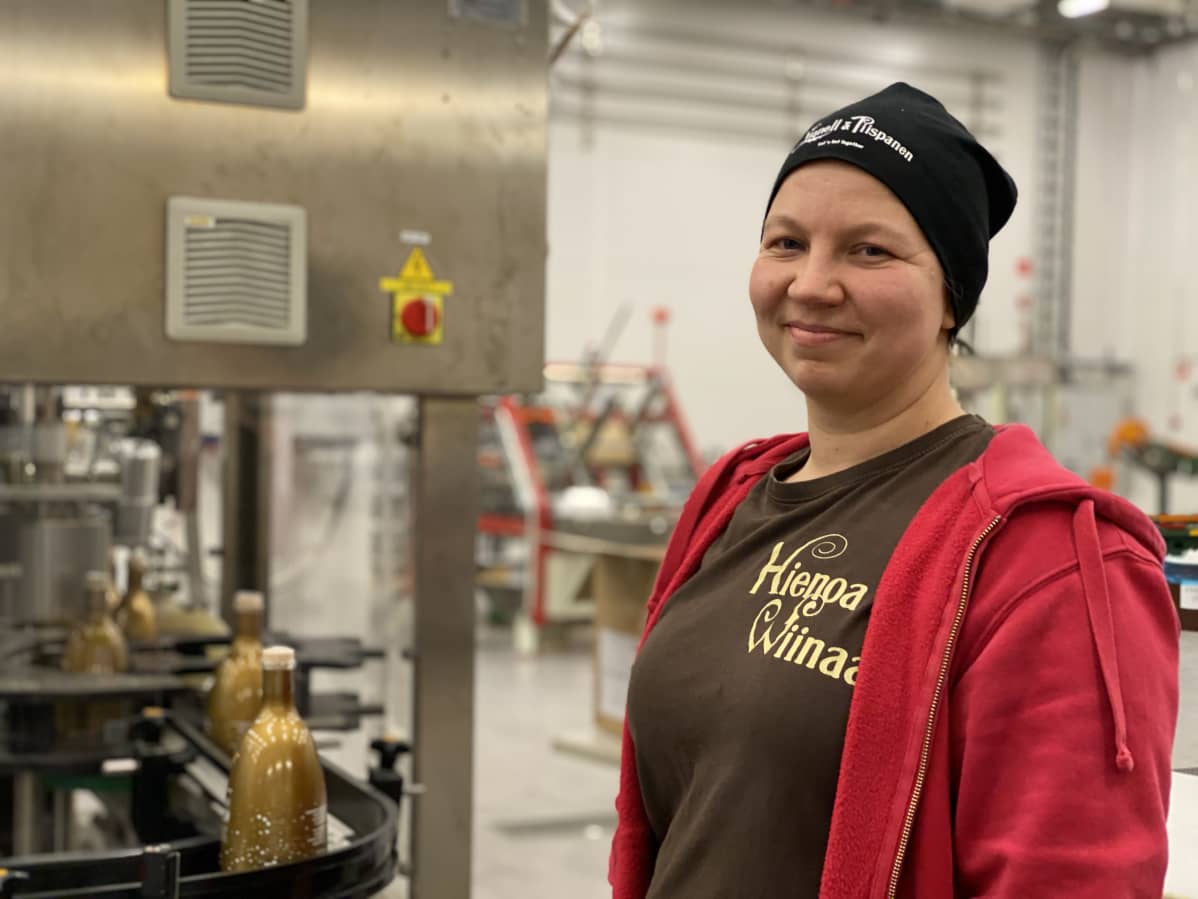 Tiina Koponen seisoo pullotuskoneen vieressä.