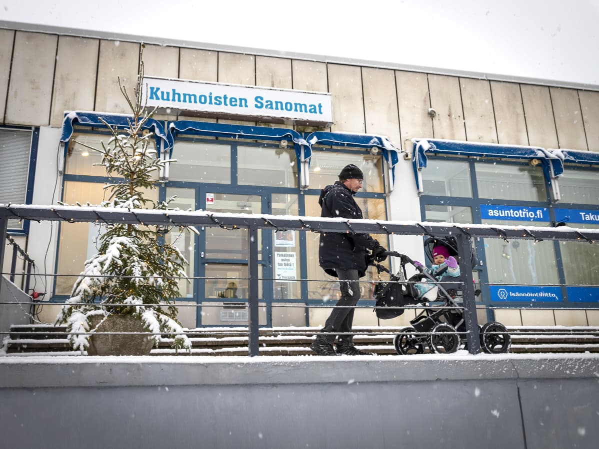 Mies ja lapsi rattaissa Kuhmoisten Sanomien toimituksen edessä.
