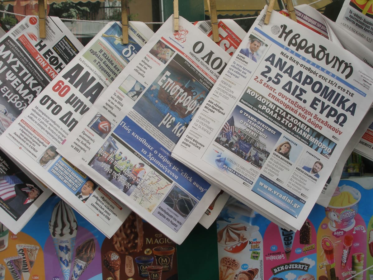 Kreikkalaisia sanomalehtiä roikkuu narulla kioskin edessä.
