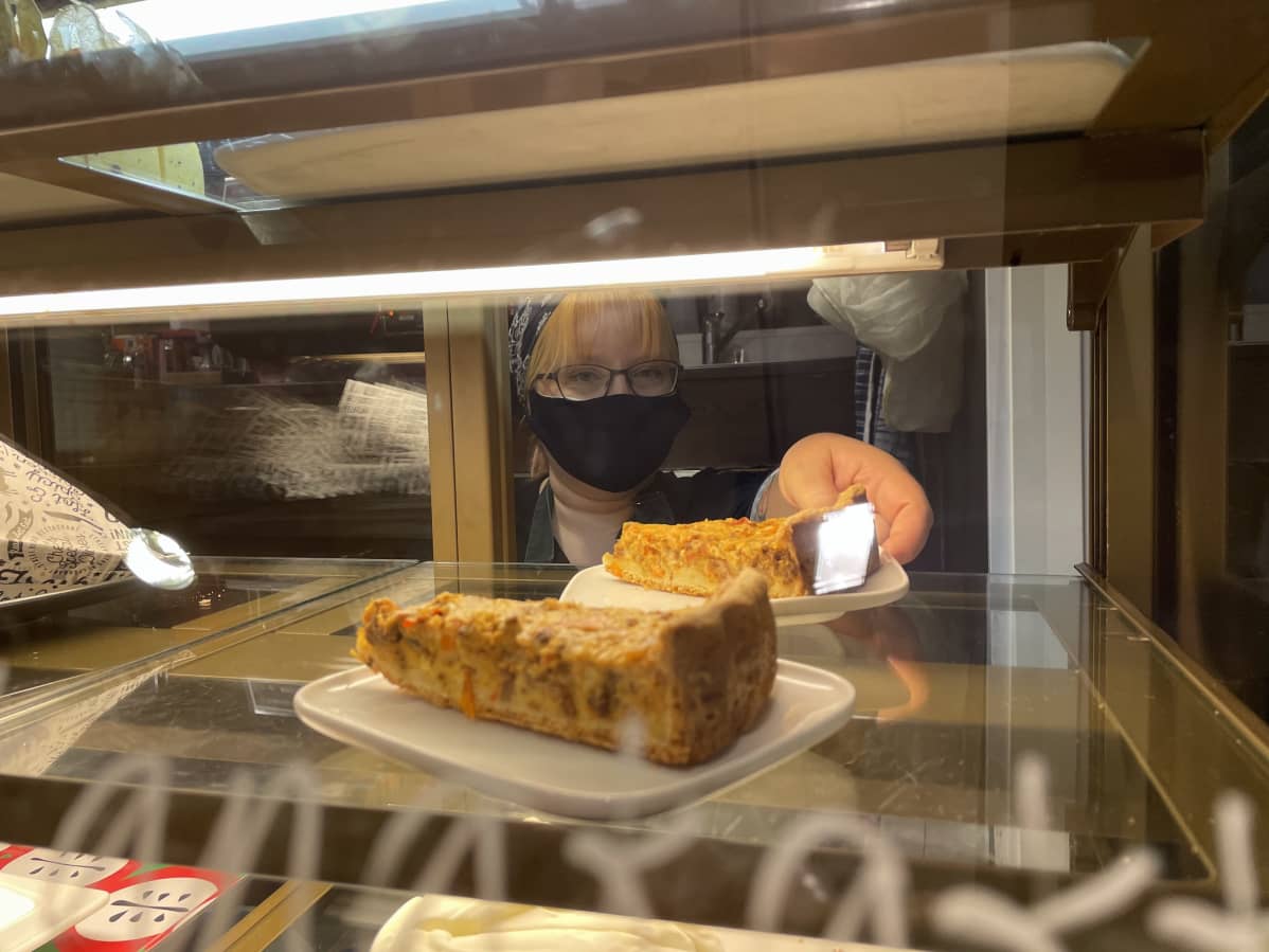 Café Murusen yrittäjä Elina Heikkinen kurkottelee porkkanakakkua vitriinistä.