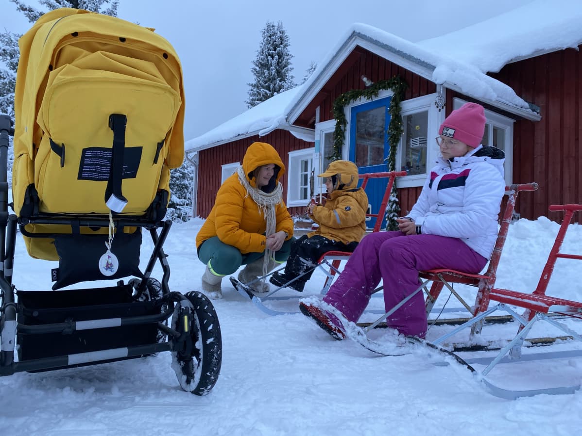 Keltaiset lastenvaunut, Anne Jäntti kyykyssä Iipon ja Millin vieressä, jotka istuvat potkureissa.