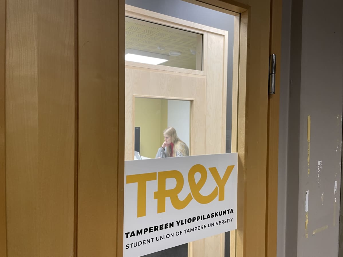 Tampereen ylioppilaskunnan lasiovi jonka läpi näkyy nainen läppärin äärellä.