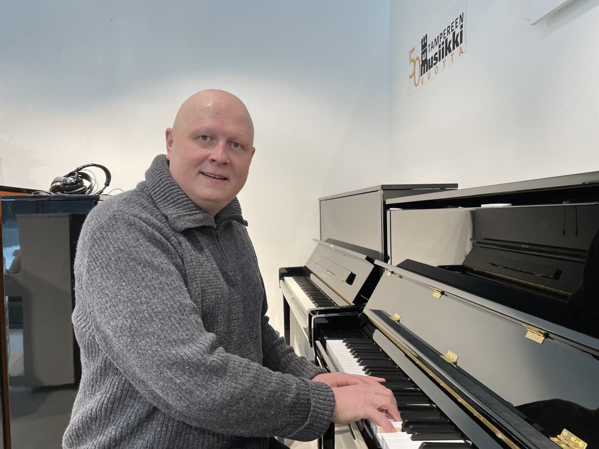 Keski-ikäinen mies soittaa pianoa ja katsoo kameraan.