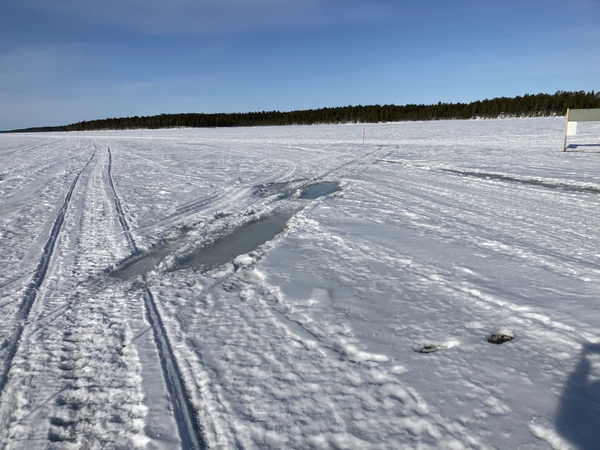 Jäällä olevalle kelkkareitille on noussut vettä. Taivas on sininen ja aurinko paistaa.