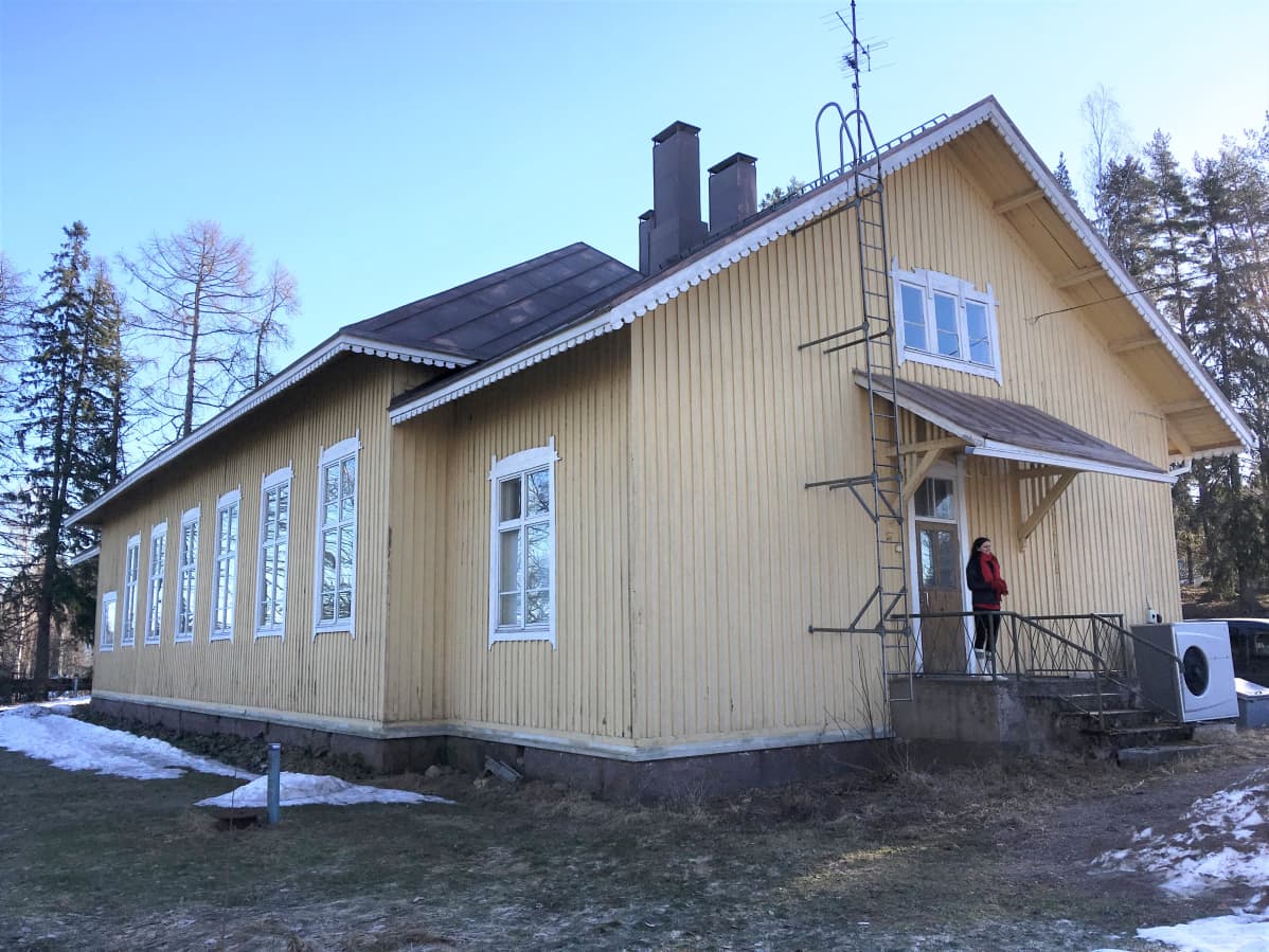 Vanha hirsitalo, jonka portailla seisoo nainen.