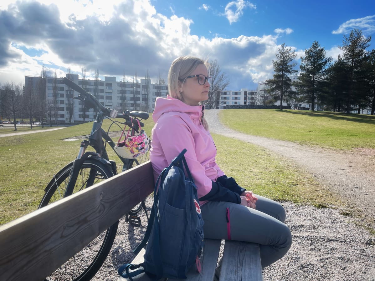 Mari Reunanen istuu puistonpenkillä, takanaan polkupyörä.