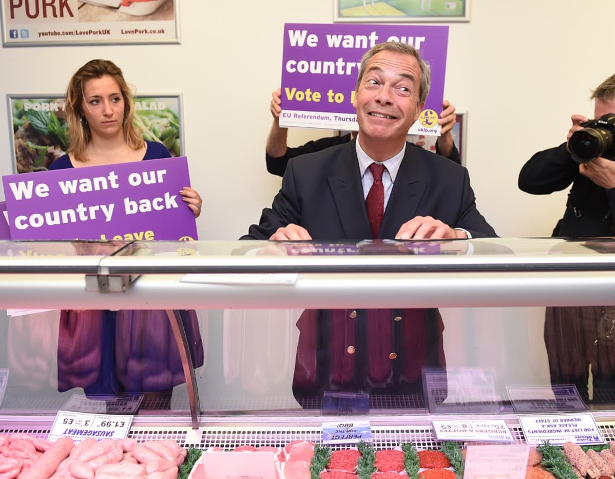 Nigel Farage ilmeilee lihatiskin takana. Vieressä kannattajia, joiden kylteissä lukee englanniksi: "Haluamme maamme takaisin".