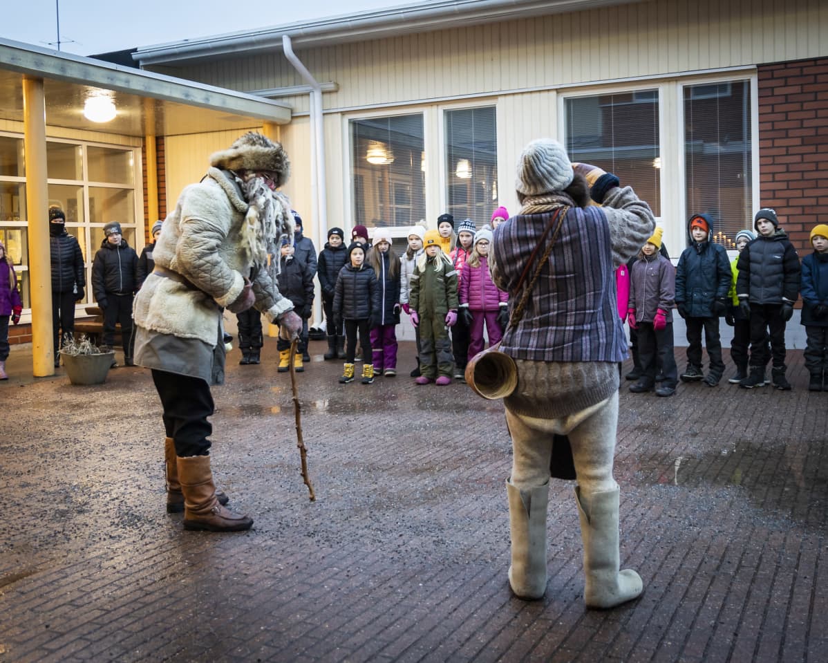 Harmaa pukki ja tonttu esiintyvät lapsille koulun pihalla.