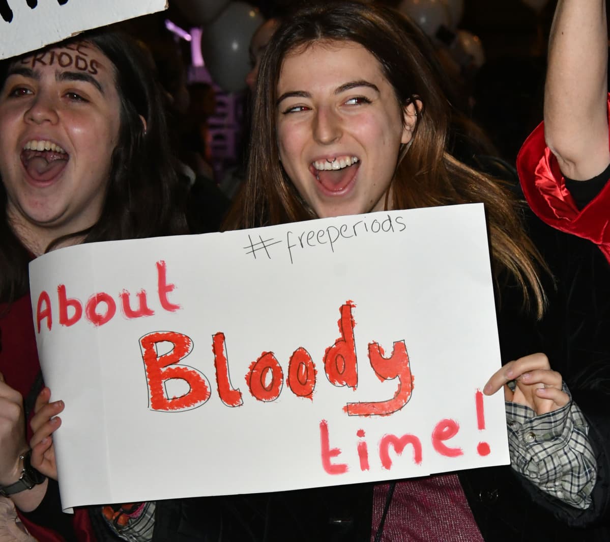 Nainen pitelee kylttiä, jossa lukee: "About bloody time".