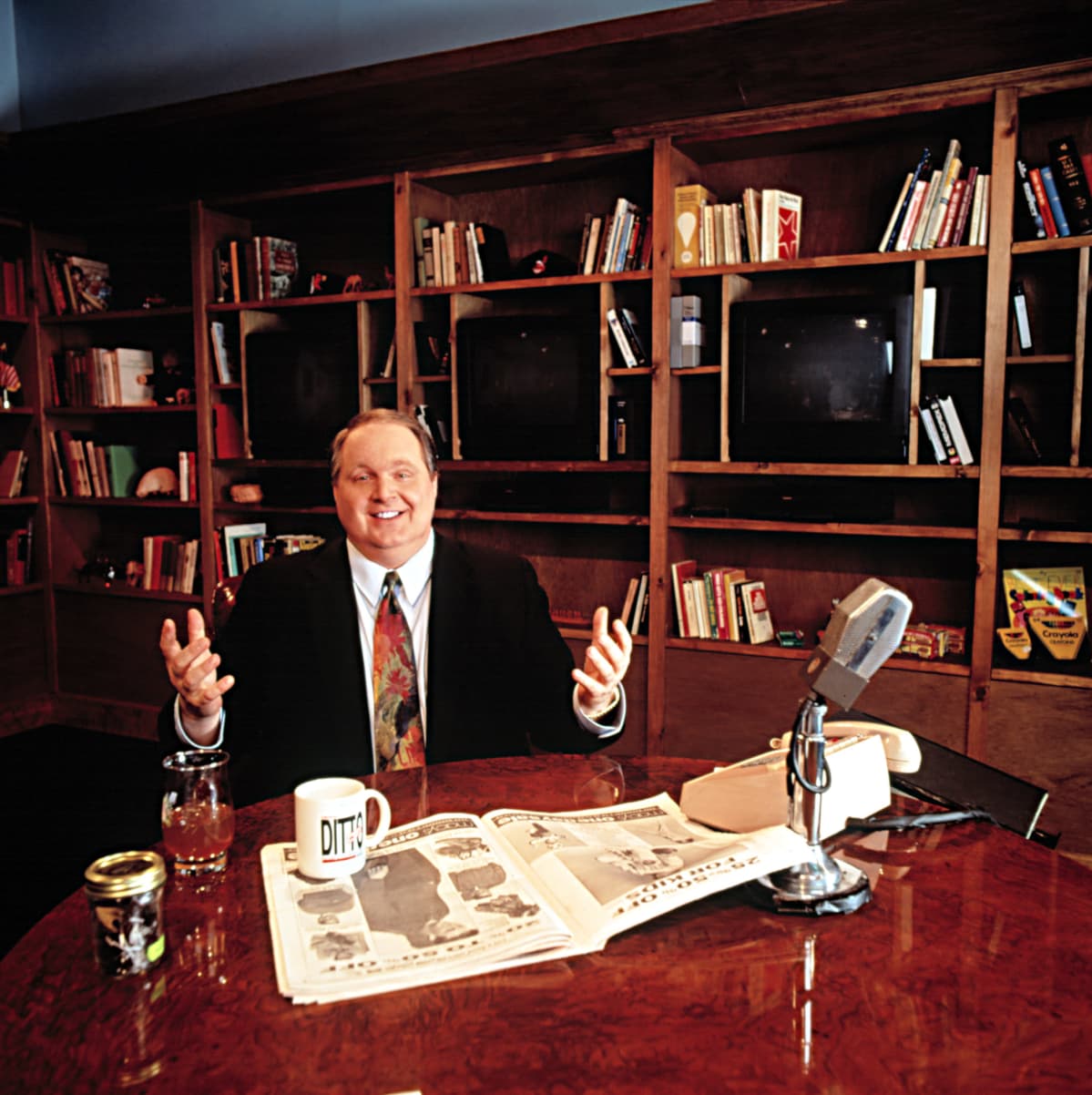 Radiotoimittaja Rush Limbaugh pöydän ääressä jossa radiomikrofoni ja sanomalehti.