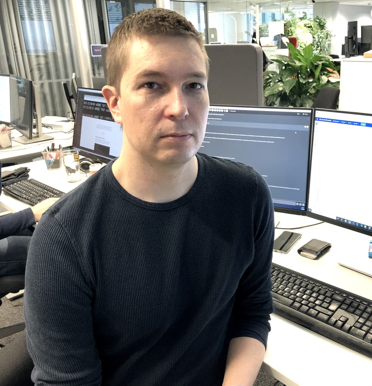 Mies istuu tietokoneen vieressä ja katsoo kameraan.