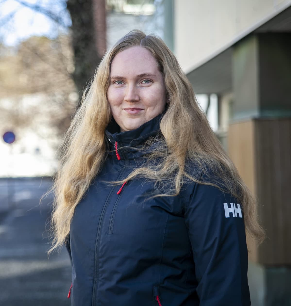 Venla Kärkkäinen katsoo suoraan kameraan kerrostalon pihalla.