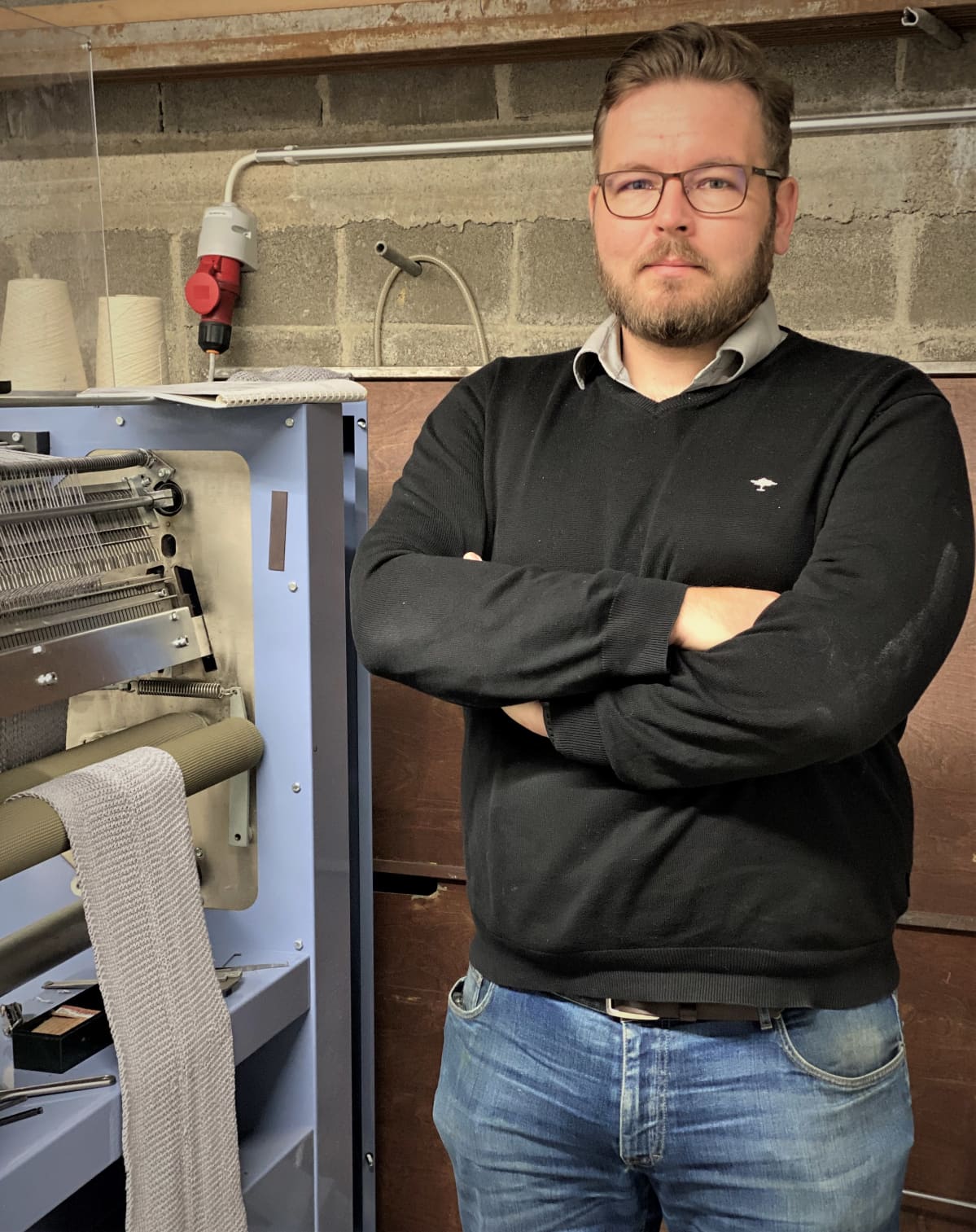 Tehtaanjohtaja Juha Haapasaari seisoo neulekoneen vieressä