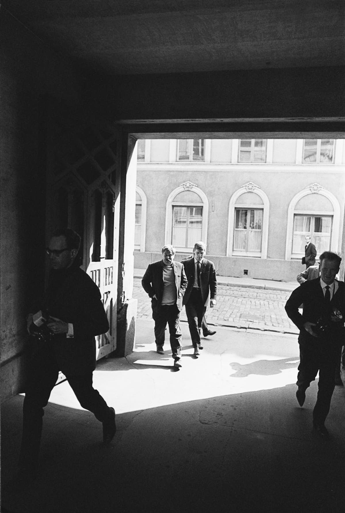 Jumalanpilkkaoikeudenkäynti Helsingin raastuvanoikeudessa. Kirjailija Hannu Salama ja Kustannus Oy Otavan toimitusjohtaja Kari Reenpää vastaamassa oikeudessa "Juhannustanssit"-romaanista nostettuun jumalanpilkkasyytteeseen. Hannu Salama raastuvan portilla, rinnalla juoksee lehtikuvaajia.