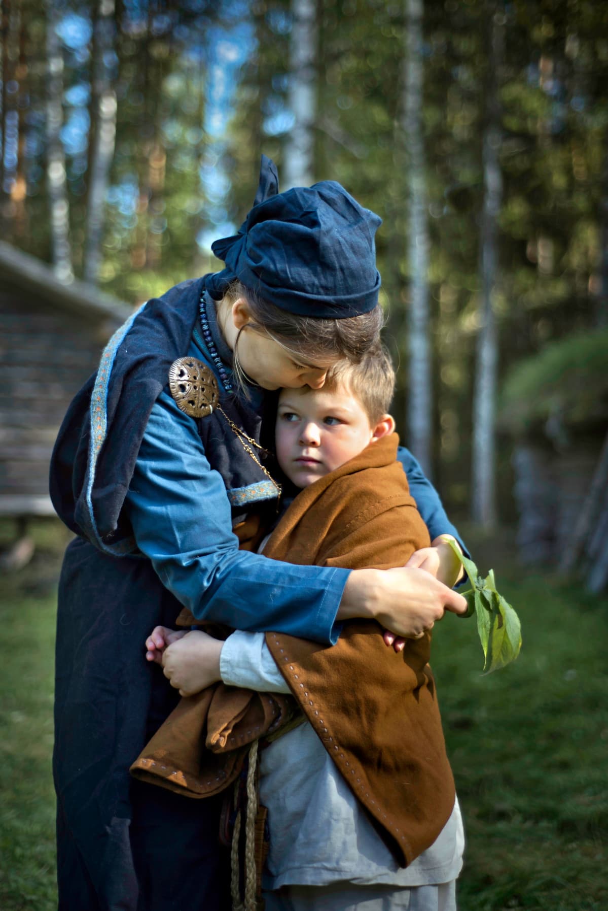 Viikinkiajan asuun pukeutunut äiti rutistaa poikaansa sylissään.