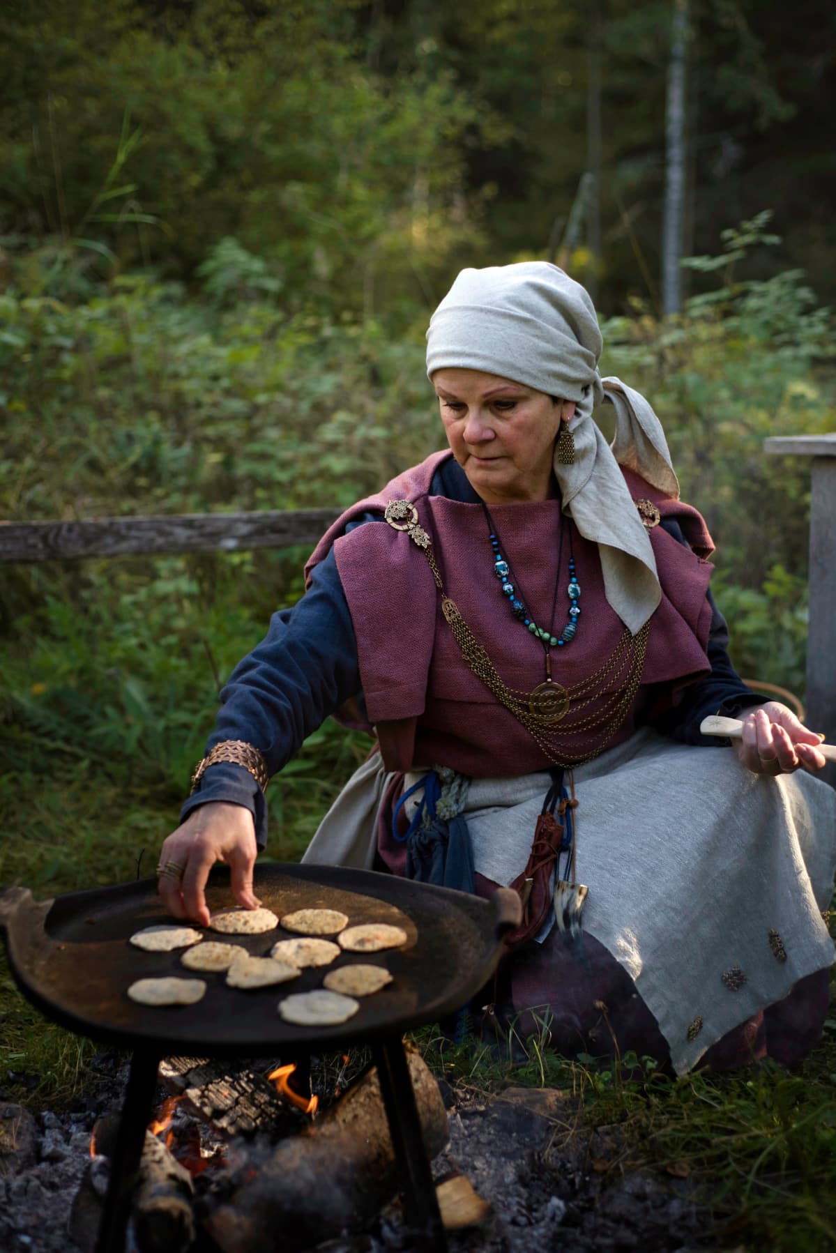 Rautakautiseen asuun pukeutunut nainen paistaa leipäsiä.