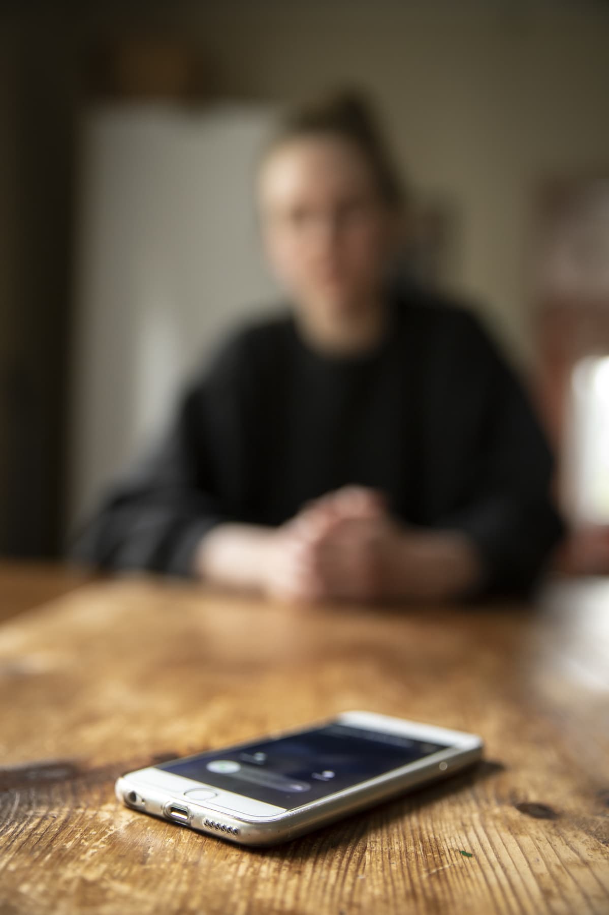 Puhelin soi pöydällä, ihminen näkyy taustalla sumennettuna.